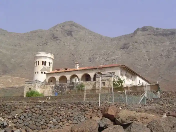 "Vista frontal de la misteriosa Villa Winter, una histórica mansión ubicada en la isla de Fuerteventura, Canarias, rodeada por un paisaje árido y montañoso que realza su aura de misterio."
