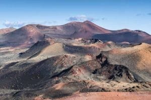 Paisaje volcánico de las Montañas del Fuego en Lanzarote, con cráteres y colinas de tonos rojizos y oscuros.