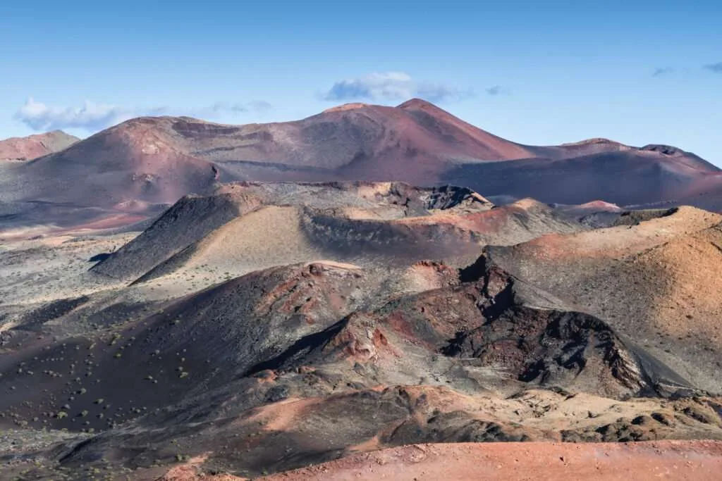 Paisaje volcánico de las Montañas del Fuego en Lanzarote, con cráteres y colinas de tonos rojizos y oscuros.