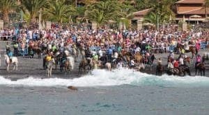 Multitud reunida en la playa de Adeje, Tenerife, durante la festividad de San Sebastián con caballos en el agua. historia de las fiestas de san sebastian en adeje
