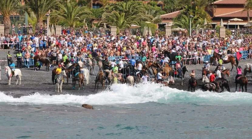 Multitud reunida en la playa de Adeje, Tenerife, durante la festividad de San Sebastián con caballos en el agua. historia de las fiestas de san sebastian en adeje