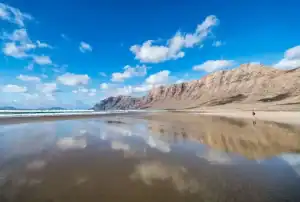 "Vista panorámica de la Playa de Famara, Lanzarote, con sus extensas arenas doradas y el impresionante macizo de Famara al fondo. Un destino ideal para los amantes del surf y la naturaleza en estado puro."