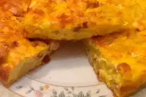 La imagen muestra una tortilla de papas casera con trozos de jamón o bacon, cortada en porciones. Su aspecto dorado y jugoso resalta la textura esponjosa del interior, que mezcla los ingredientes de manera uniforme, aportando un toque de sabor adicional al plato tradicional.