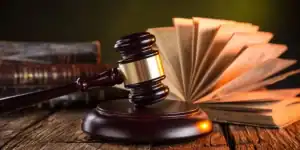 Imagen de un mazo judicial sobre una mesa de madera, acompañado de un libro de leyes abierto en el fondo, simbolizando la justicia y el derecho penal.