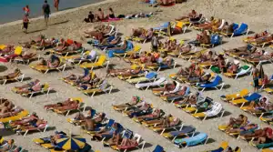 "Turistas disfrutando del sol en tumbonas, alineados en la playa en la costa de las Islas Canarias."