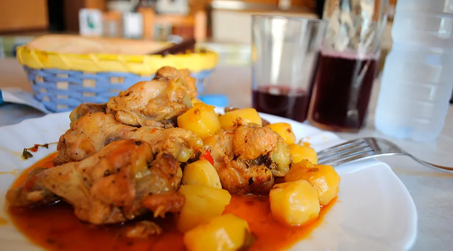 Plato de conejo en salmorejo con papas, acompañado de un vaso de vino tinto en un guachinche canario.