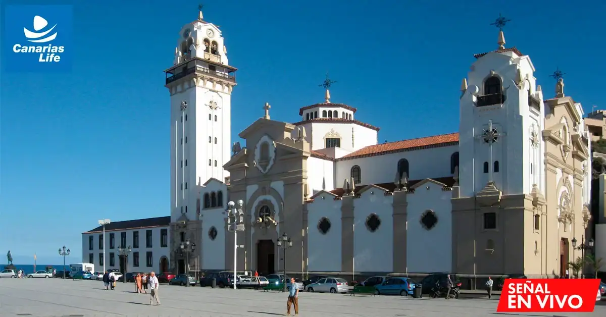 Iglesia colonial con torre alta, arquitectura blanca y terracota, plaza abierta, mar visible en el horizonte, clima soleado.
