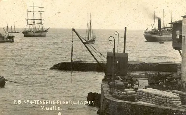 Puerto de La Cruz, Tenerife historica: barcos y muelle con grúa, actividad portuaria.
