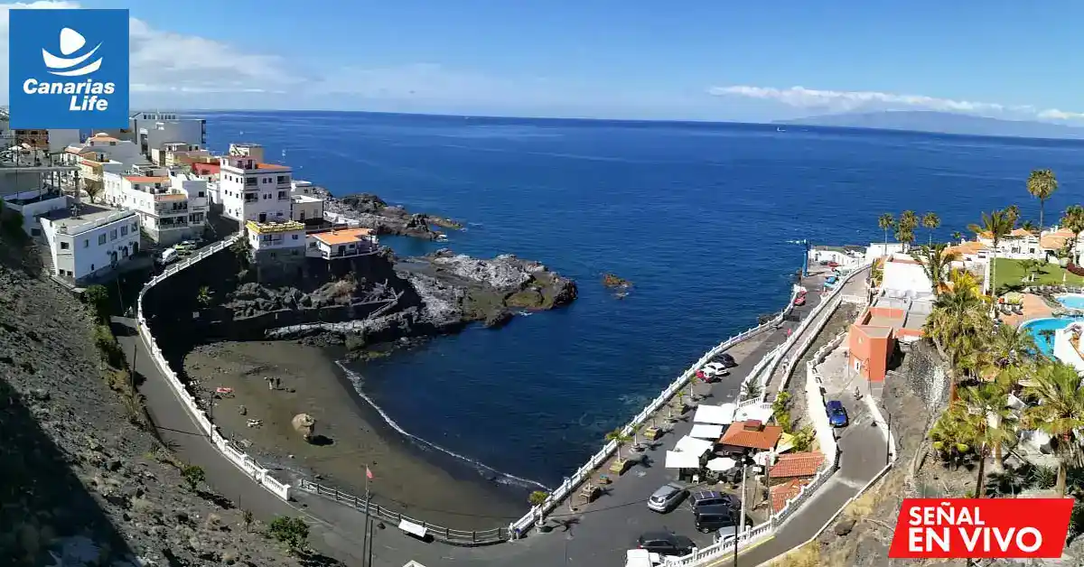 Pueblo costero con edificios blancos, playita pequeña, mar azul, palmeras y piscina, paisaje tropical.