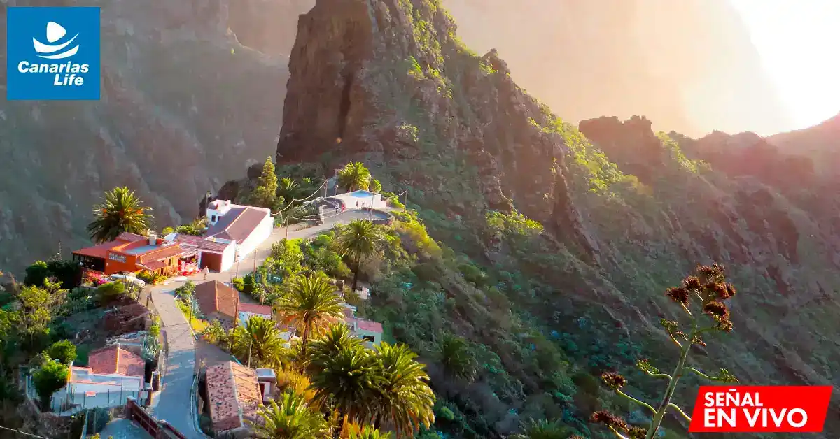 Pueblo costero con casas blancas rodeado de montañas verdes, paisaje natural y soleada.