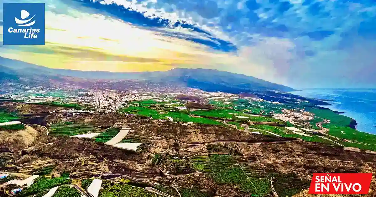 Panorámica de la costa canaria con campos verdes, urbanizaciones y mar, bajo un cielo despejado.
