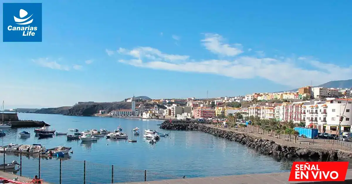 Puerto con barcos, edificios coloridos, mar azul, cielo despejado; paisaje costero vibrante.