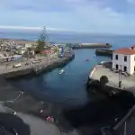 Puerto con buildings, marina, vehicles, y playas cercanas; paisaje costero con mar y nubes claras.