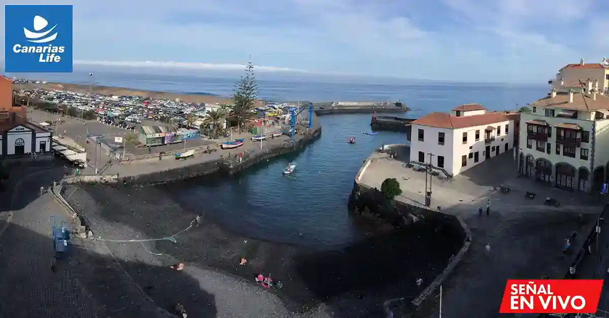 Puerto con buildings, marina, vehicles, y playas cercanas; paisaje costero con mar y nubes claras.