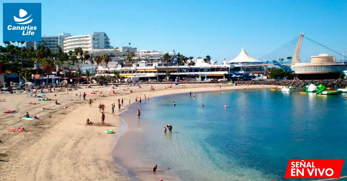 Playa con turistas, edificios modernos, puente colgante y estructura circular; paisaje tropical con palmeras y mar cristalino.