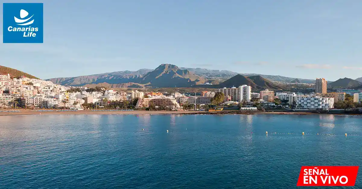 Paisaje costero con mar azul, montañas en el fondo y urbanización a lo largo de la costa.