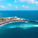 Paisaje costero con edificios, playas negras y mar azul, probablemente en una isla del archipiélago canario.