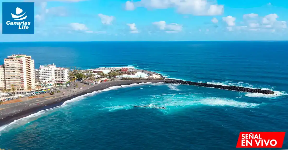 Paisaje costero con edificios, playas negras y mar azul, probablemente en una isla del archipiélago canario.