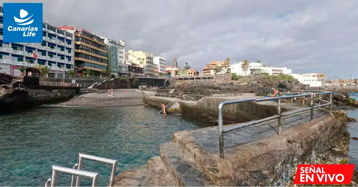 Piscina natural en la costa, con edificios detrás y gente nadando, en un entorno urbano costero.