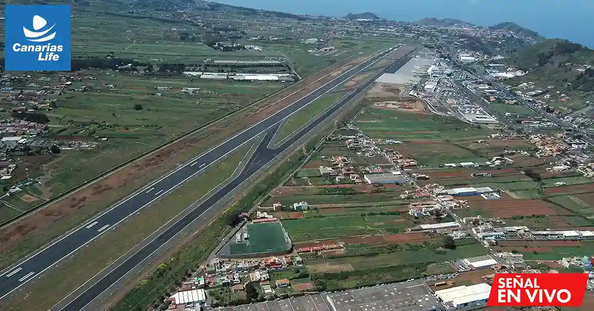 Vista aérea de la pista de un aeropuerto con las zonas urbanas y agrícolas circundantes, con el logotipo de «Canarias Life» en la esquina superior izquierda y un indicador de emisión en directo en la parte inferior derecha.