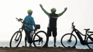 Tres ciclistas con cascos celebran en una playa, con bicicletas a su lado.