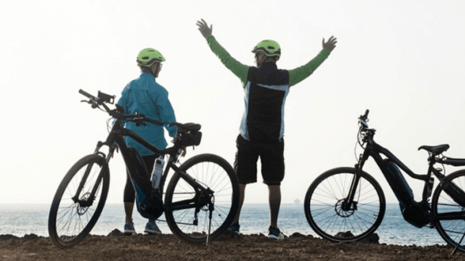 Tres ciclistas con cascos celebran en una playa, con bicicletas a su lado.