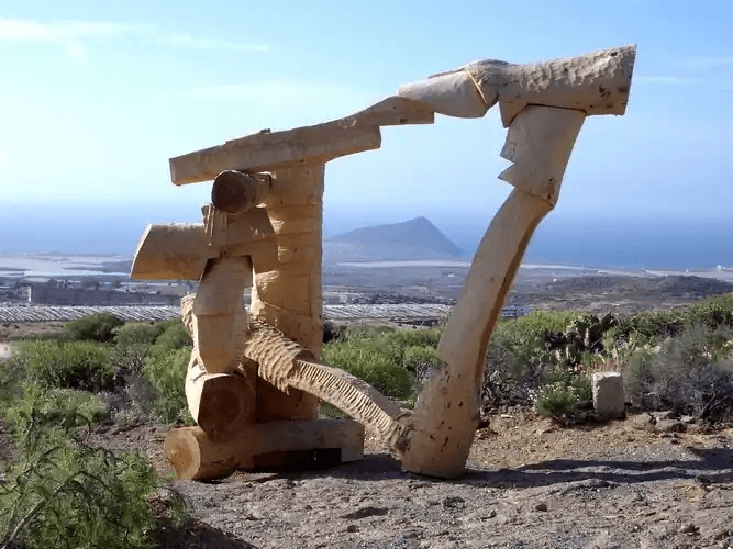 San Isidro – Arte y Naturaleza en Los Cardones. Escultura de madera en una vista panorámica con mar y montaña en el fondo, en un entorno natural.