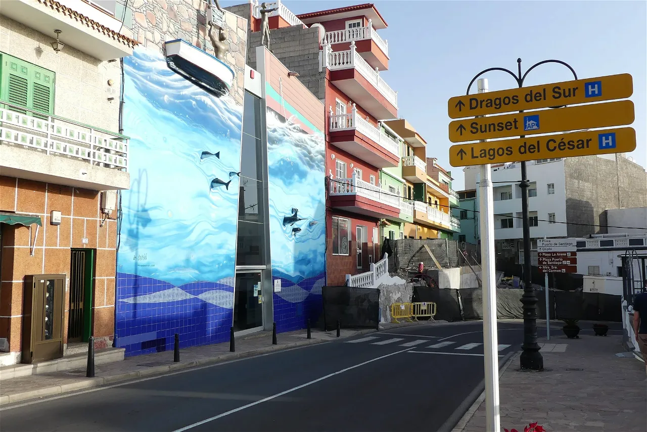 Fachada del Museo del Pescador en Puerto Santiago, decorada con un mural que muestra un paisaje marino con olas y peces, además de una pequeña embarcación real colocada en la parte superior de la pared, integrando elementos tridimensionales.