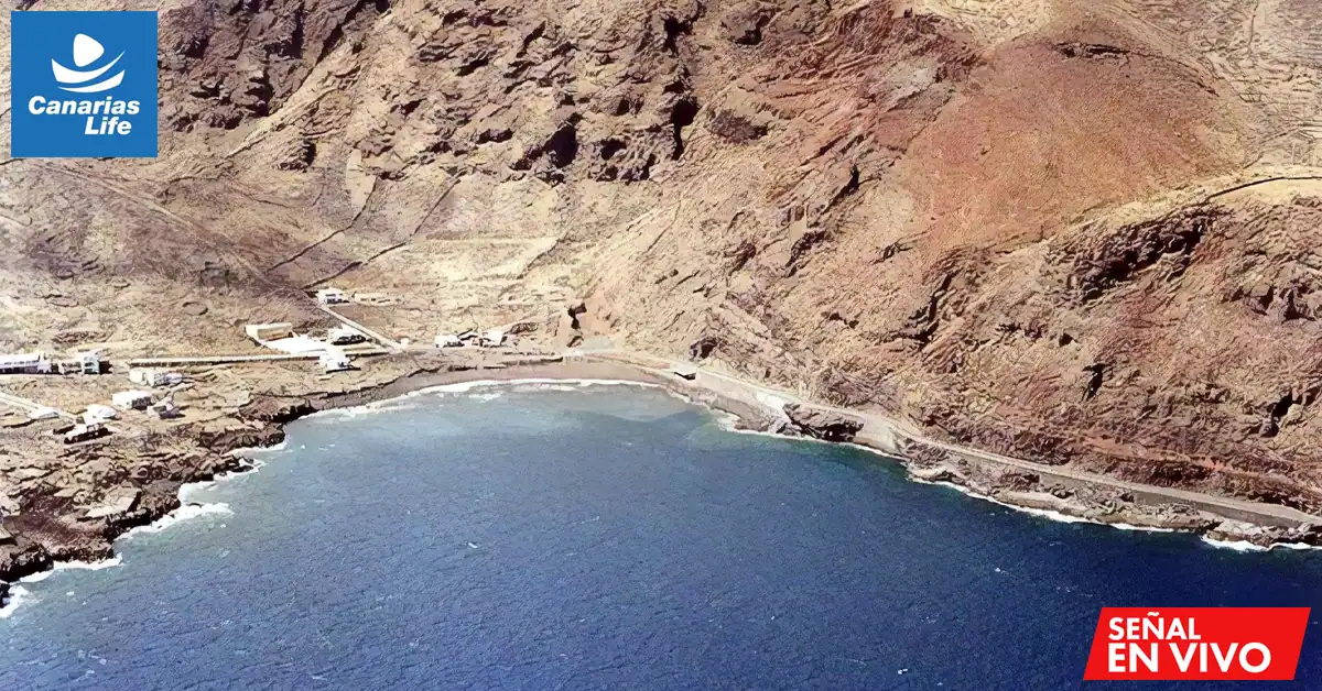 Vista aérea de la playa de Timijiraque en Valverde, Islas Canarias. La imagen muestra una playa de arena dorada rodeada de paisaje volcánico, con el océano Atlántico de color azul intenso al fondo y algunas personas caminando cerca de la orilla.