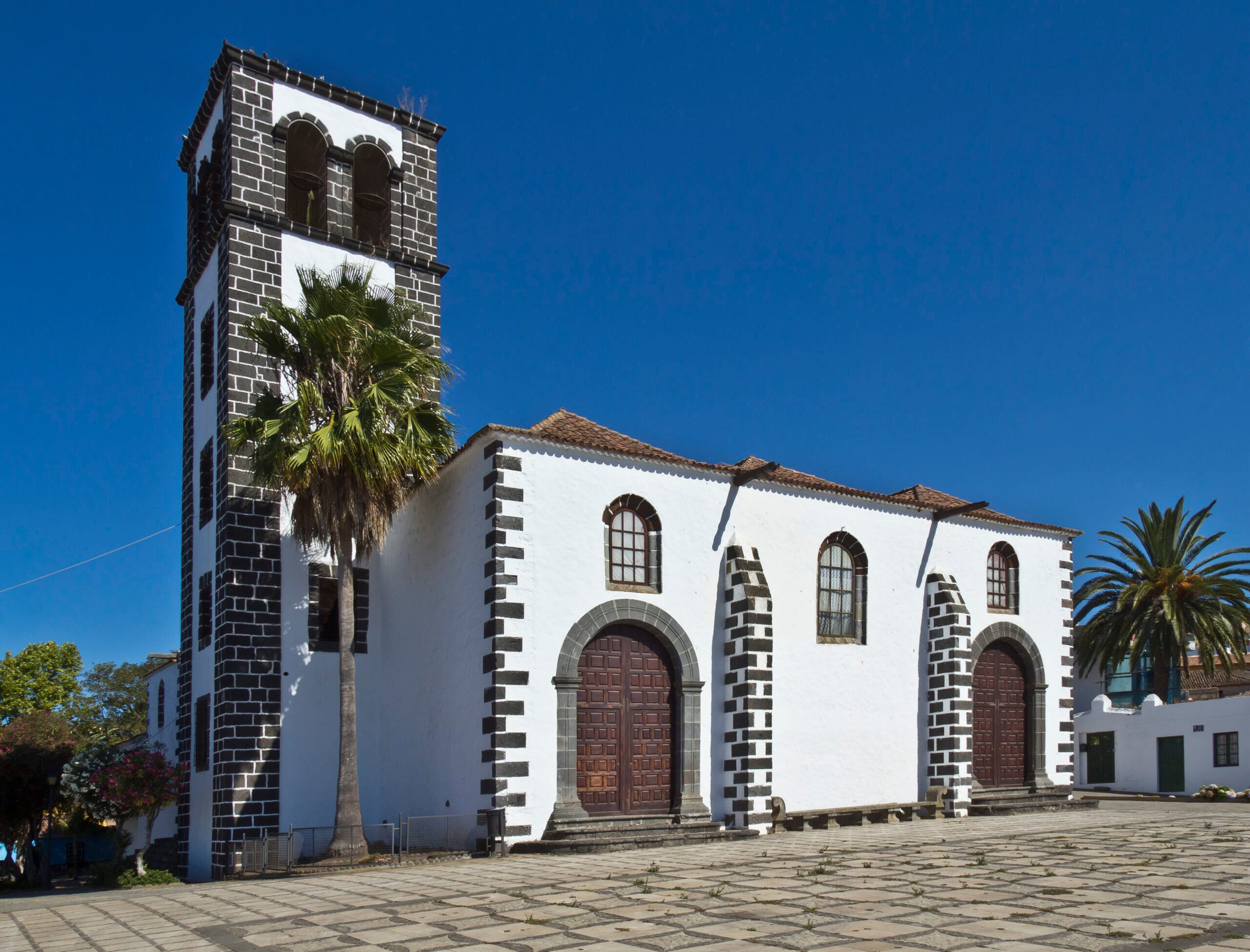 Iglesia Santa Catalina Martin de Alejandría Iglesia colonial con torre, arcos y ventanas, palmadas, cielo azul, plaza abierta.