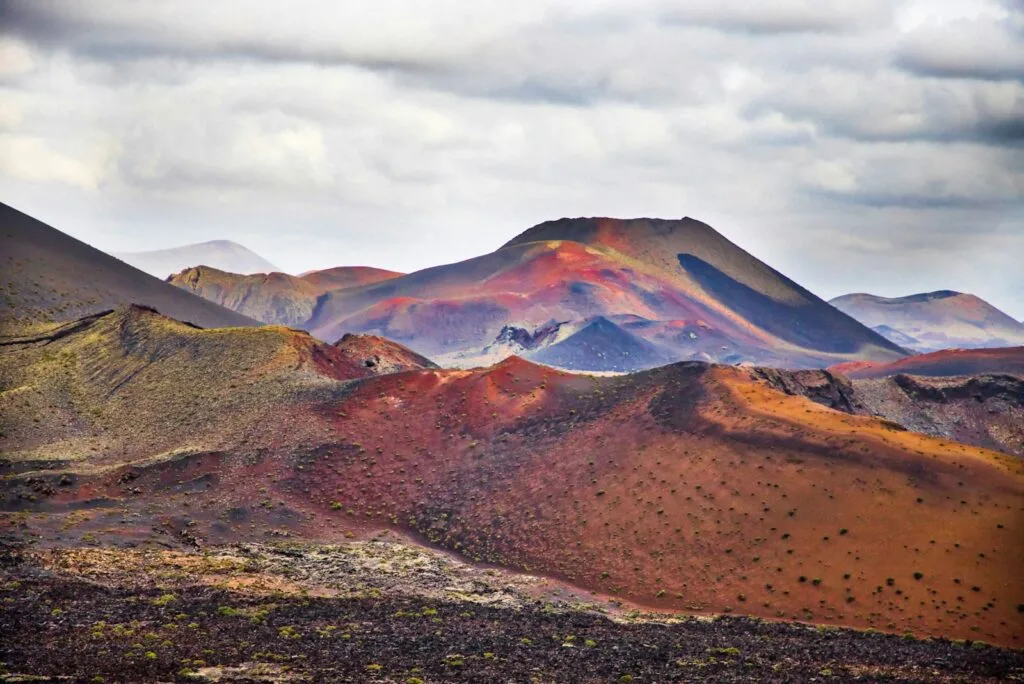 Photo by Josep Castells Desiertos rojizos con montañas coloridas bajo una nube gris, paisaje lunar.