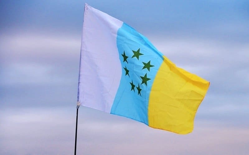 Bandera blanca, azul y amarilla con estrellas verdes;