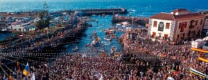 Puerto lleno de personas y barcos en la costa de Canarias durante un evento festivo.