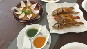 Plato de pescado frito, salsa verde y naranja, y una taza con cebollas y hierbas.