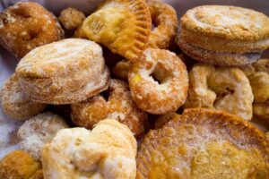 Dulces fritos cubiertos con azúcar, variados en forma y tamaño, probablemente pastelillos o rosquillos.