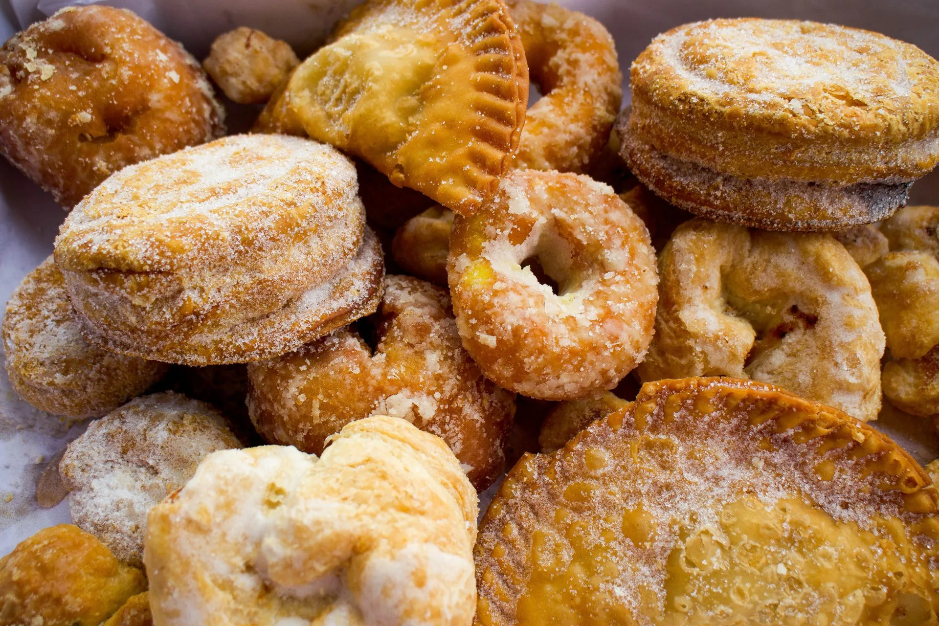 Dulces fritos cubiertos con azúcar, variados en forma y tamaño, probablemente pastelillos o rosquillos.