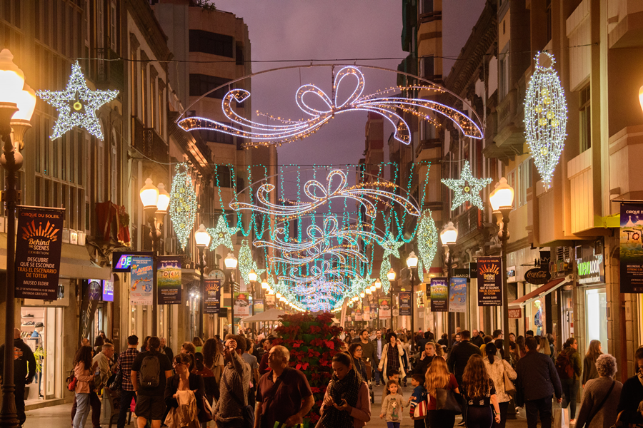 Festiva calle llena de gente, iluminada con decoraciones navideñas y luces.