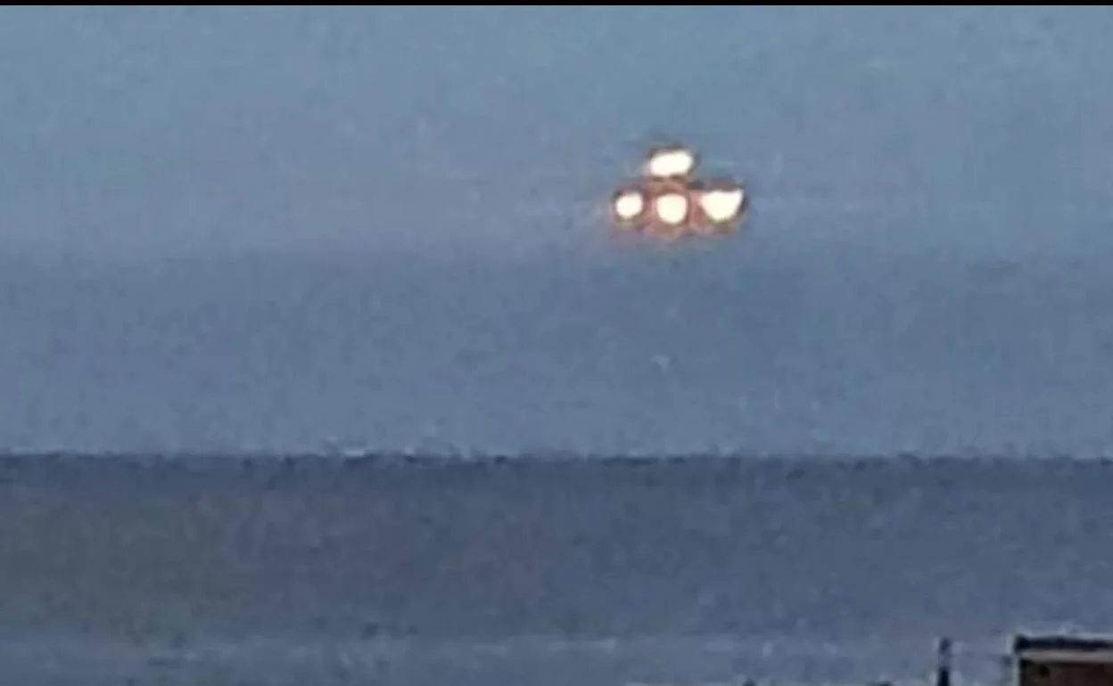 Objeto luminoso en el cielo nocturno o crepuscular, compuesto por cuatro luces brillantes agrupadas en una formación triangular o cuadrada difusa. El fondo es un cielo azul grisáceo con una línea horizontal que podría ser el horizonte marino o terrestre. La imagen está tomada a distancia y con baja resolución, lo que dificulta identificar el objeto con certeza —podría tratarse de un avión, dron, satélite, o simplemente un efecto óptico o de movimiento.