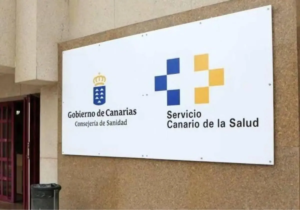 Cartel en la pared de un edificio con los logotipos del Gobierno de Canarias y del Servicio Canario de la Salud, junto a una entrada con puerta abierta.