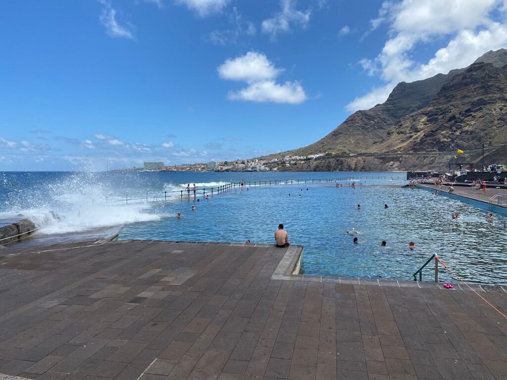 Bañistas en las piscinas naturales de Bajamar con olas rompiendo en el muro exterior, Tenerife