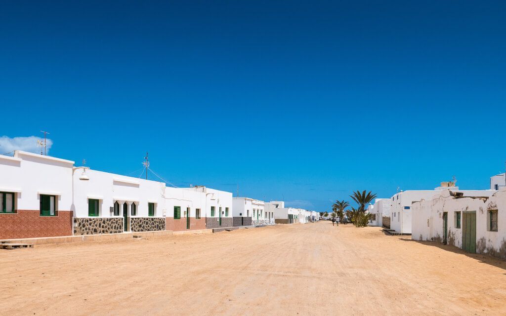 Calles de arena de Caleta del Sebo con casas blancas y barcas en el puerto de La Graciosa, Lanzarote