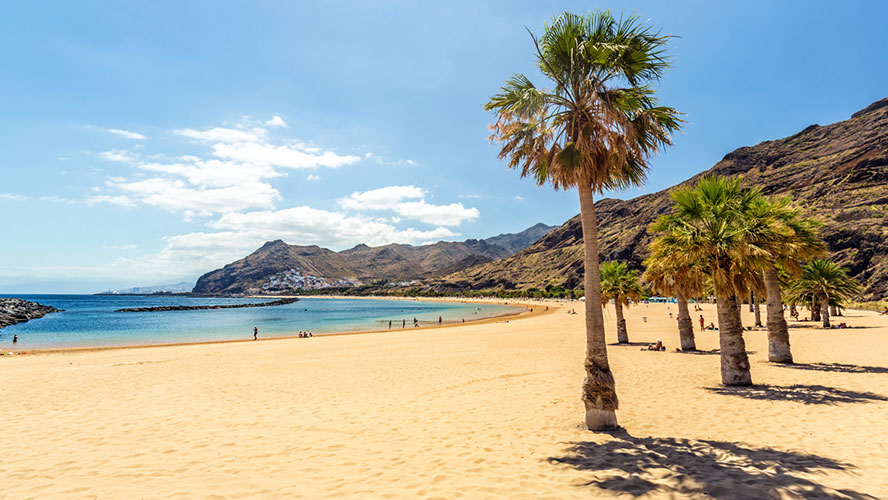 Palmeras y arena dorada de Las Teresitas al atardecer con el Atlántico y las montañas de Anaga, Tenerife