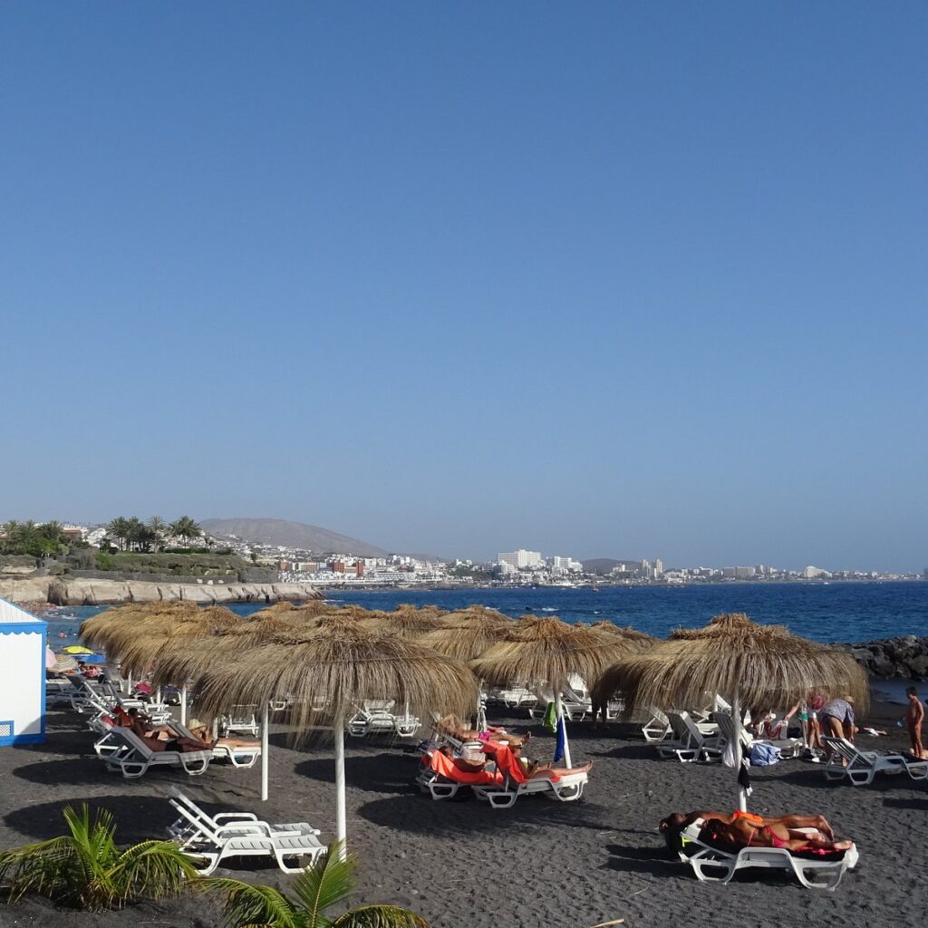 Arena oscura y aguas turquesas de la Playa El Beril en la Bahía del Duque Norte Costa Adeje Tenerife