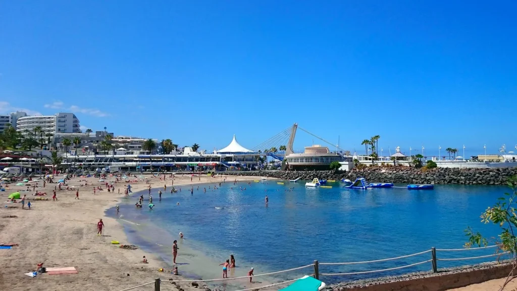 Arena dorada de la playa turística Playa La Pinta en Costa Adeje con Puerto Colón al fondo Tenerife