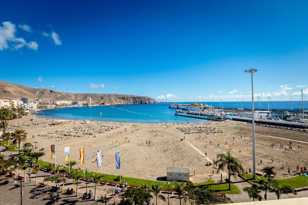 Vista de la Playa de Los Cristianos con arena dorada, aguas tranquilas y el puerto al fondo, Arona, Tenerife